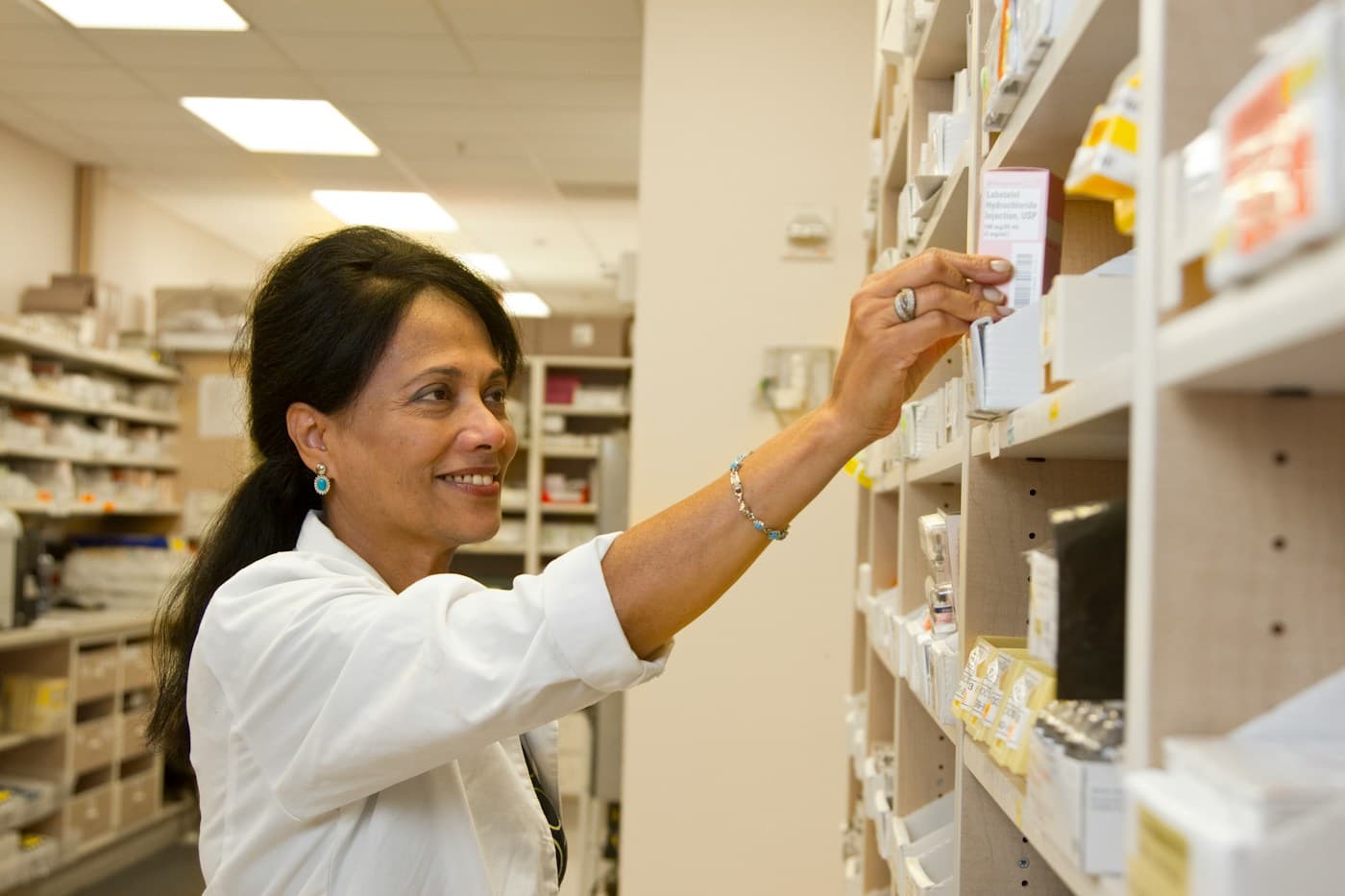 A pharmacist reaching for a medicine box on a pharmacy shelf